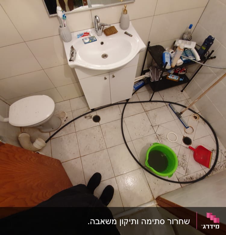 חדר אמבטיה עם דלי ירוק וצינור על הרצפה